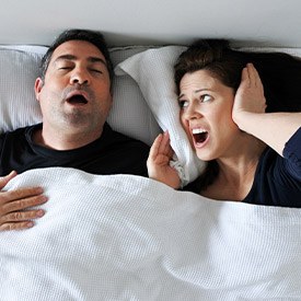 Woman covering ears next to snoring man