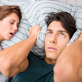 Man covering ears next to snoring woman