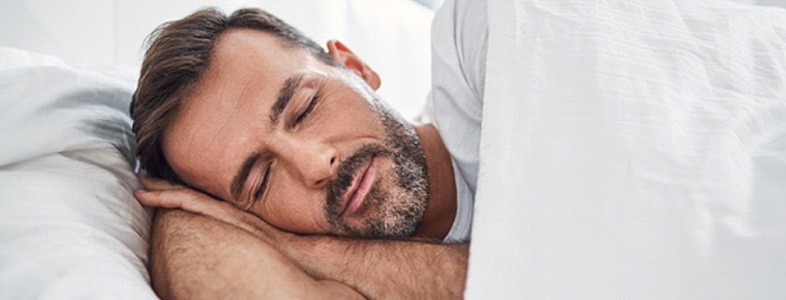 A middle-aged man asleep in his bed after undergoing sleep apnea therapy in Fort Worth