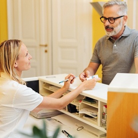 A male patient handing paperwork over to a female receptionist who is answering questions about insurance