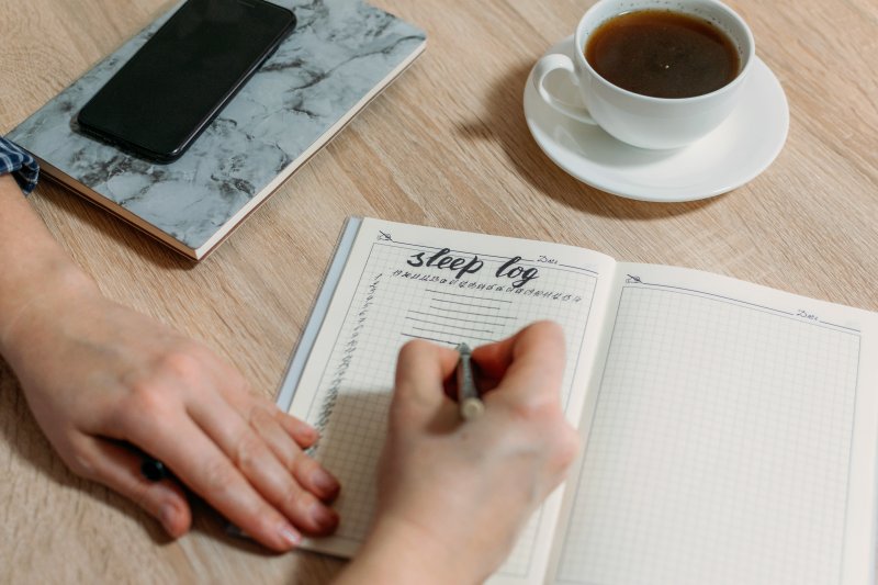 Writing in sleep log on a desk with cup of tea