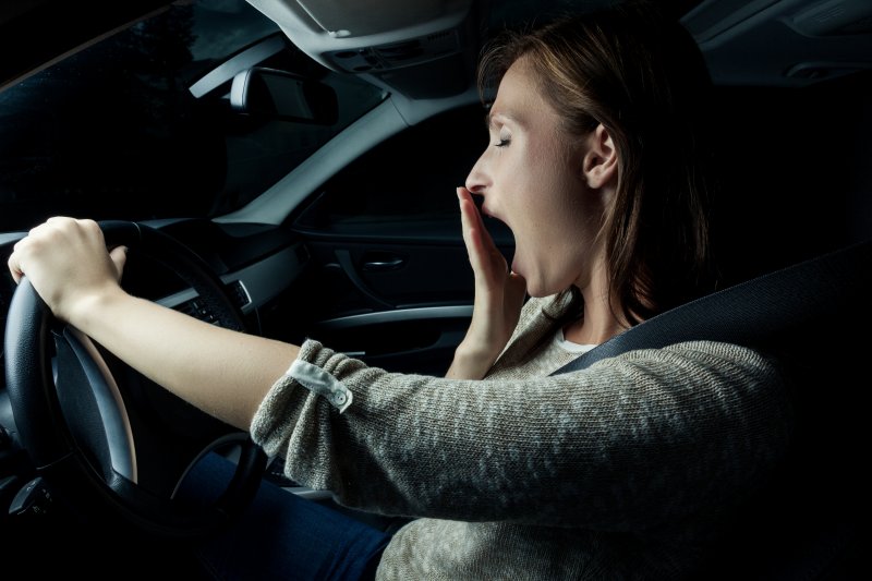 Woman yawning while holding steering wheel one-handed