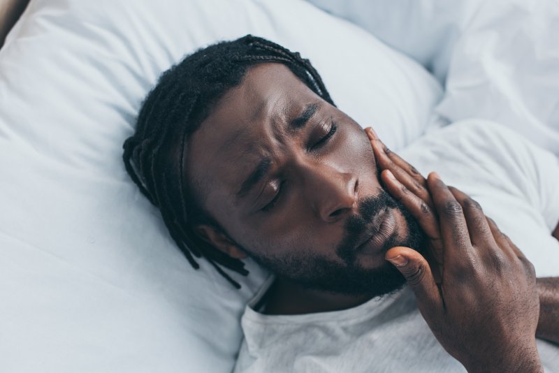 Man lying in bed feeling jaw due to TMJ pain