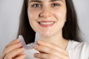 Smiling woman holding splint for TMJ pain