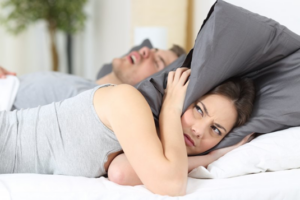 Woman pulling a pillow over her head to drown out her partner’s snoring