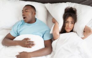 Man snoring while his wife wears frustrated expression 